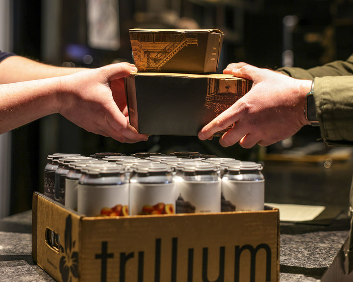 Close up image of hands exchanging Trillium food and beer takeout
