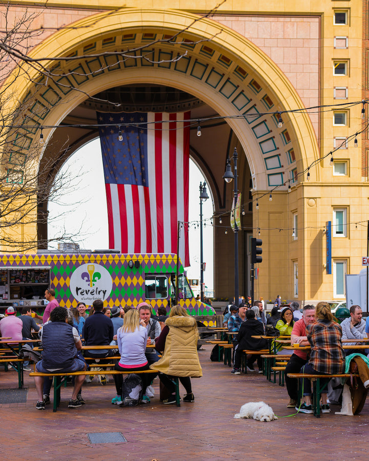 People sitting at tables at Trillium Greenway featuring a food truck and American flag in the background